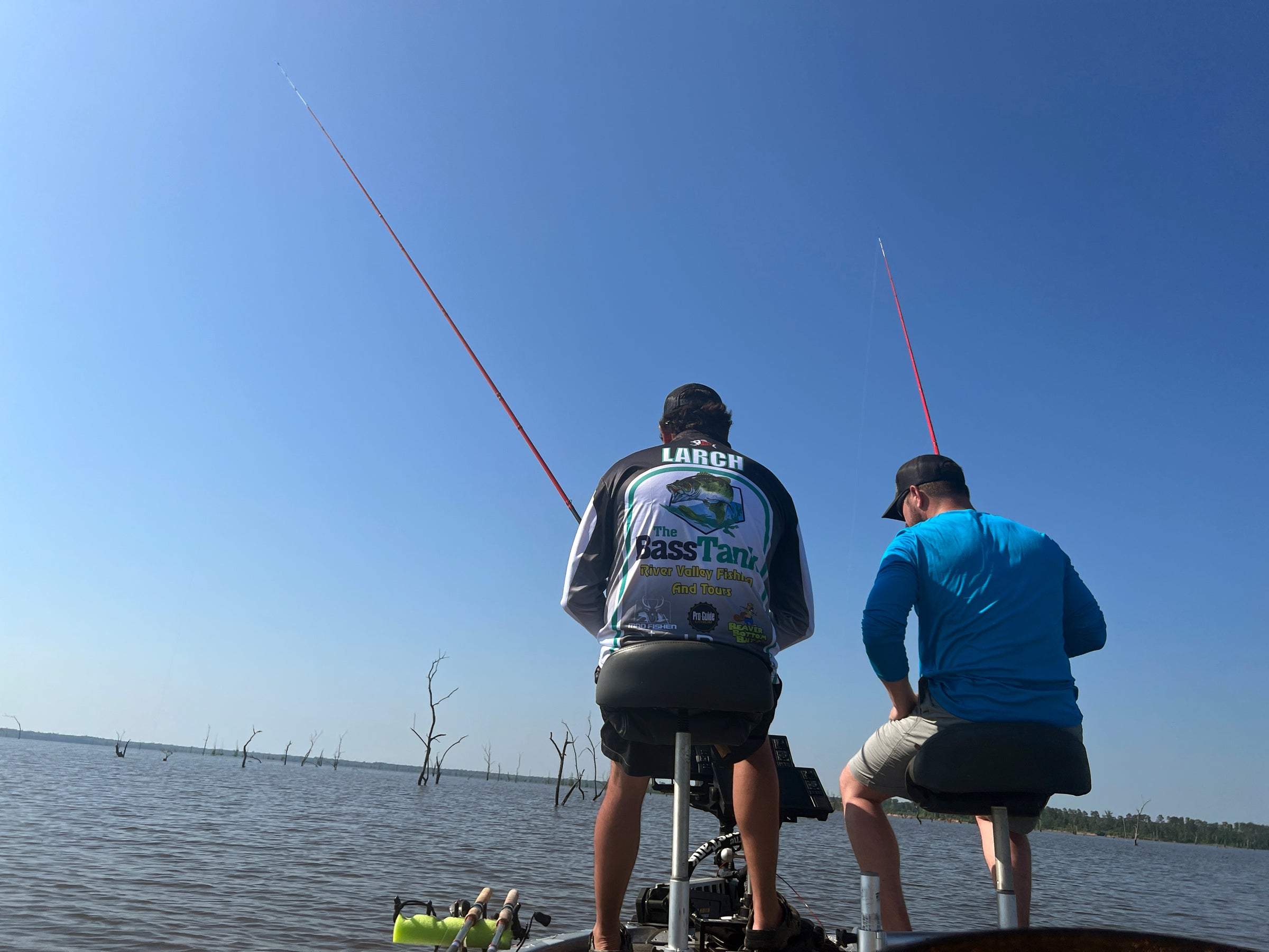 Two anglers sit on a boat, rods extended over the water, using Mad Braid braided fishing line for crappie fishing. The calm lake and distant tree stumps create a perfect fishing scene.